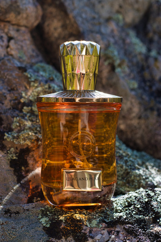 Fae Perfume Lilac and Pear perfume bottle with a faceted gold cap on a lichen-covered rock.